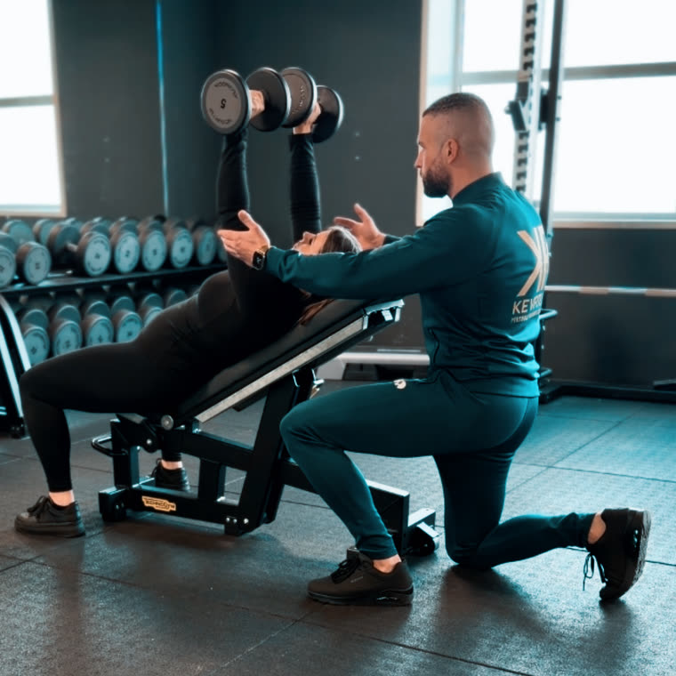 Kevin coacht een klant bij het drukken met dumbbells